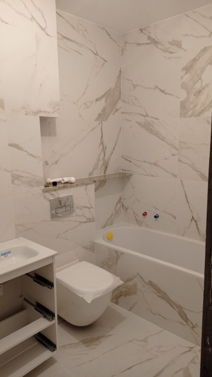 Łazienka wykończona płytkami marmurowymi z wanną i WC podwieszanym